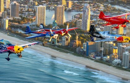 "High-flying aerobatic aircraft performing over the Gold Coast beach during the Pacific Airshow, with a crowd of spectators enjoying the show."