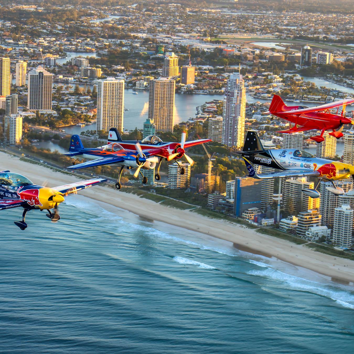 "High-flying aerobatic aircraft performing over the Gold Coast beach during the Pacific Airshow, with a crowd of spectators enjoying the show."